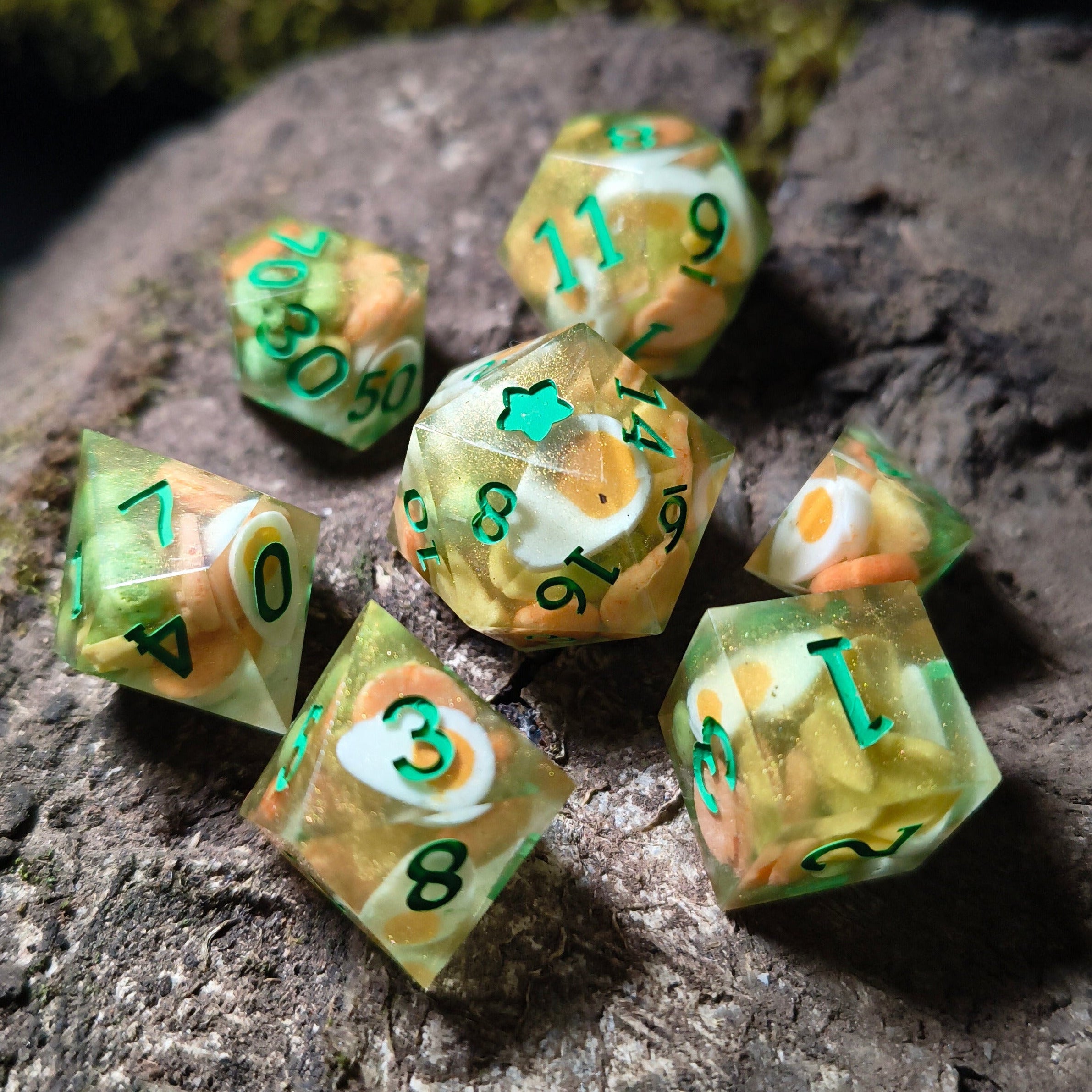 Set of green and gold polyhedral dice with egg, pea, and pineapple chunk inclusions on a wood surface