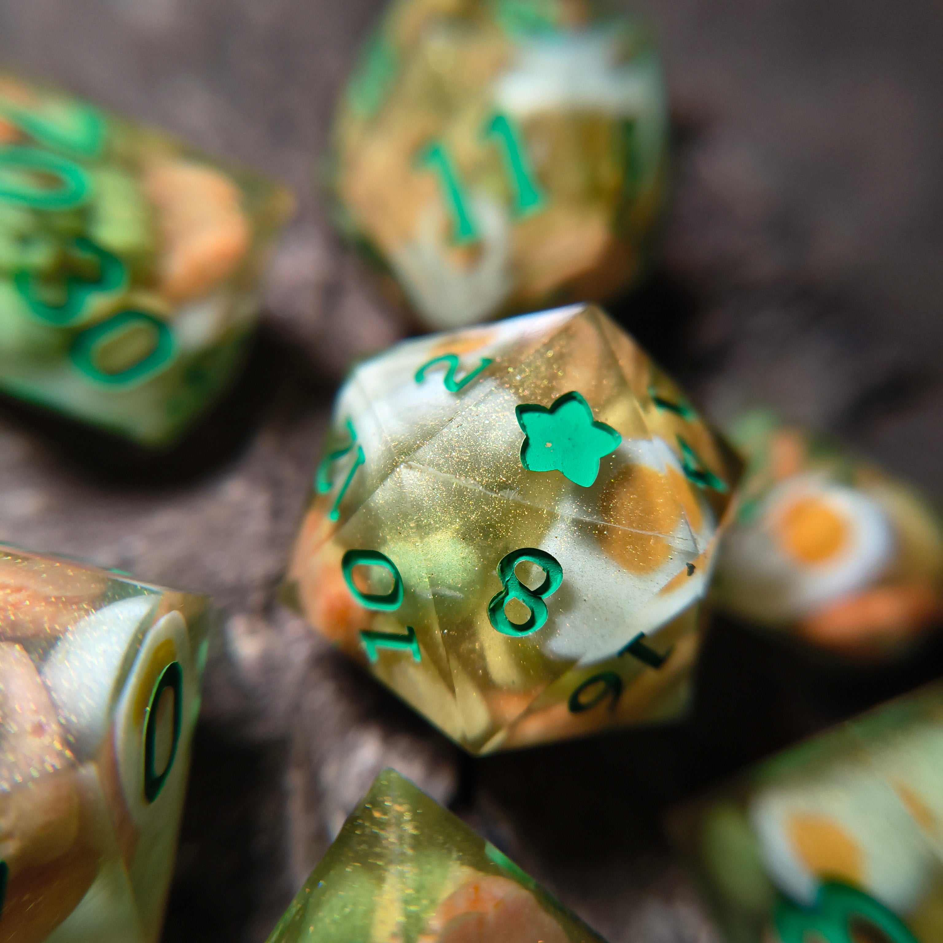 Close-up of green and gold polyhedral dice with egg, pea, and pineapple chunk inclusions on a wood surface