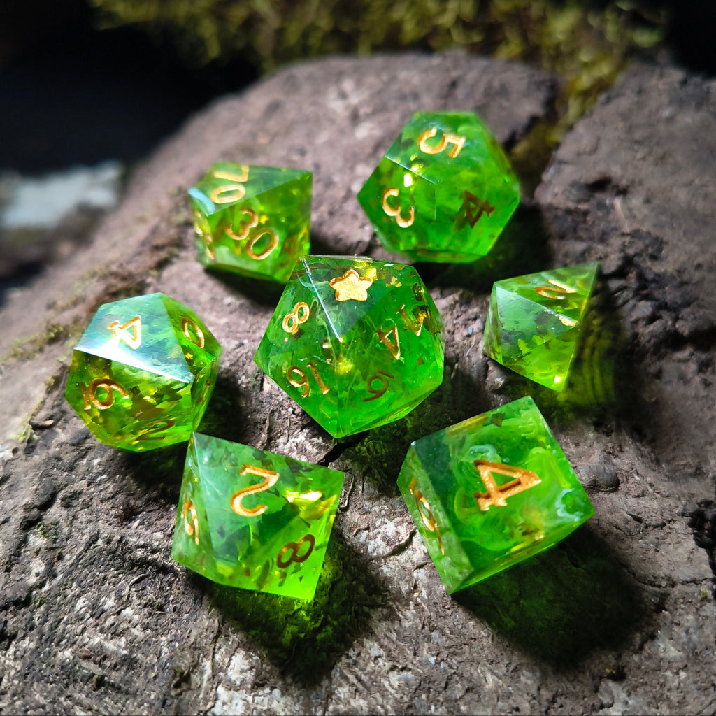 Set of green polyhedral dice with gold flakes and white swirls on a wood surface