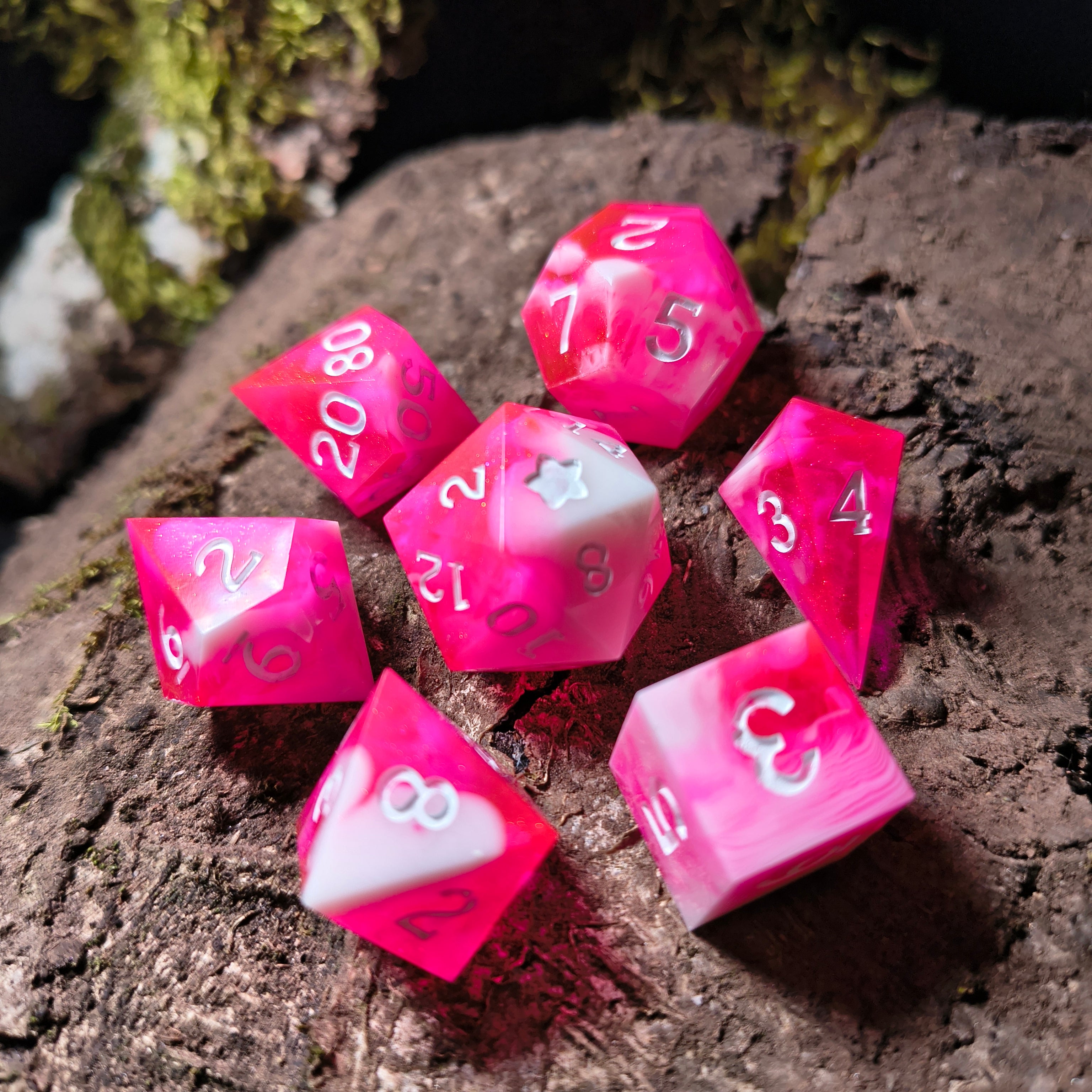 Set of pink polyhedral dice with white swirls on a wood surface